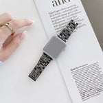 Rhombic grid ceramics replacement strap for Apple Watch resting on a magazine with a hand visible.